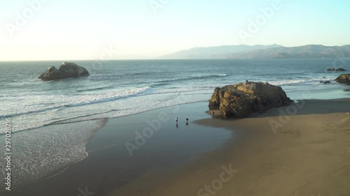 People enjoying warm weather at the beach below Cliff House in San Francisco.  Looking north from the cliffs, Marin Headlands in the distance.  Low tide, wet sand.