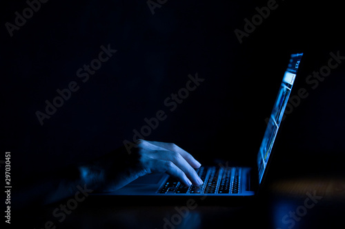 Hand of a man using laptop computer for hacking or steal data at night in office. Hacking concept photo