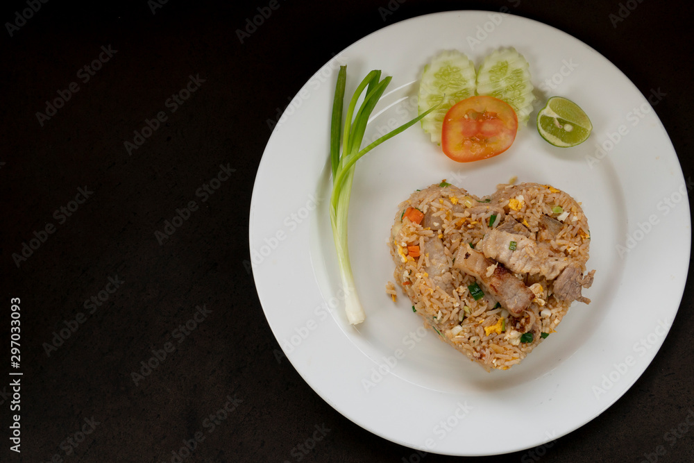 Fried rice with pork a heart shaped dish with vegetable side dishes on a white tile on a black background. Fried rice with pork a heart shaped dish with vegetable side dishes on a white tile on a black background.