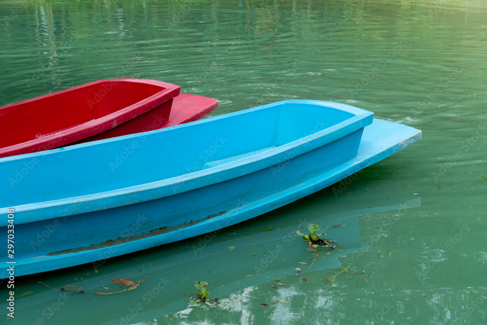 Naklejka premium Red and blue plastic boat on the beautiful green water surface.