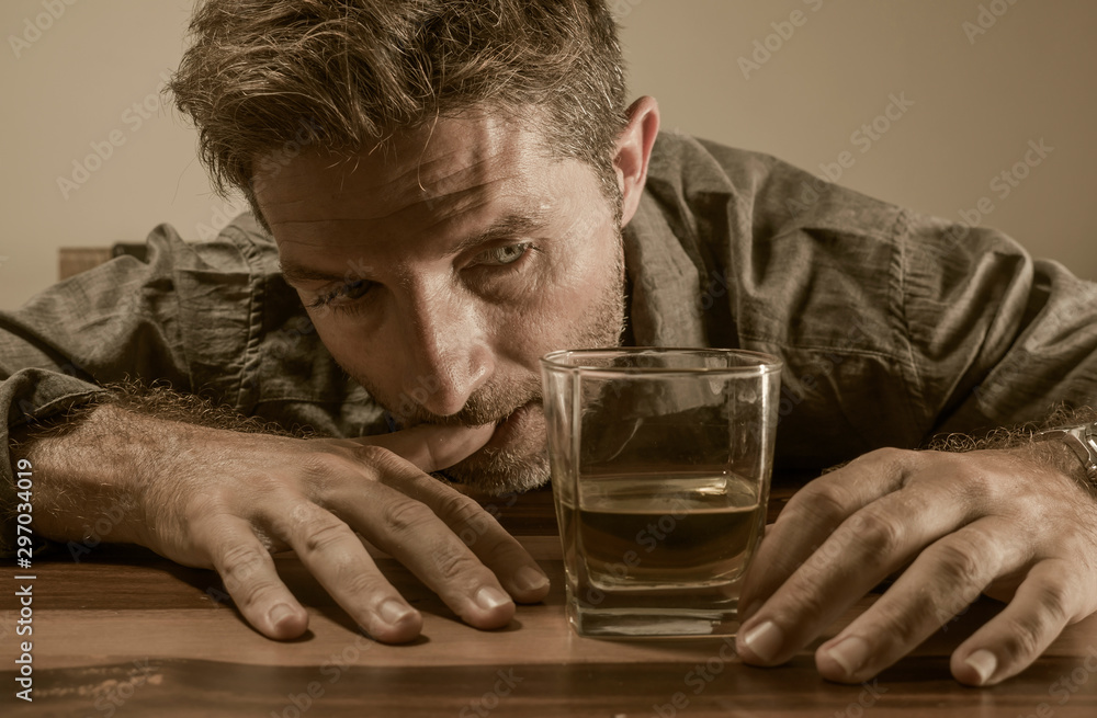 alcoholic depressed and drunk addict man sitting in front of whiskey glass trying holding on drinking in dramatic expression suffering alcoholism and alcohol addiction alcoholic depressed and drunk addict man sitting in front of whiskey glass trying holding on drinking in dramatic expression suffering alcoholism and alcohol addiction