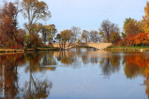 Beautiful fall landscape with a bridge in the city park.Scenic view with colored trees around old style bridge in sunlight reflected in the lake Mendota bay water. Tenney Park, Madison, Wisconsin, USA