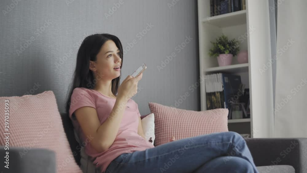 Happy girl using voice recognition on phone to record a message sitting on a couch in the night at home Happy girl using voice recognition on phone to record a message sitting on a couch in the night at home