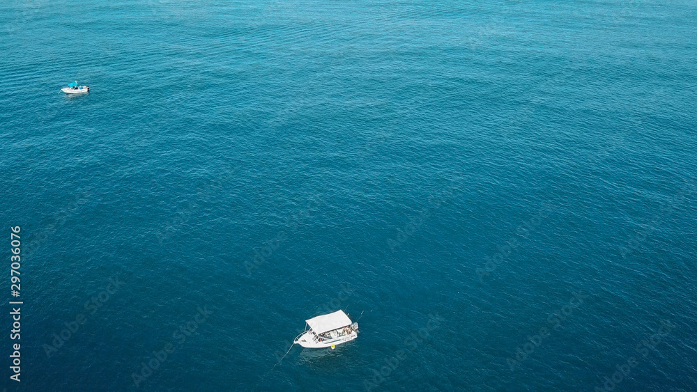 Fototapeta premium Stunning Turquoise Blue Crystal Clear Water On A Sunny Day With Small White Fishing Boat Below