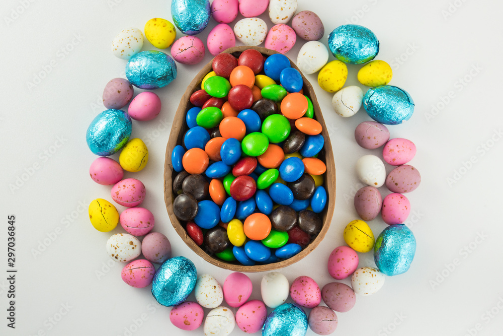 Large Chocolate Easter Egg Half Filled And Surrounded With Colorful Smaller Eggs On A White Studio Background Large Chocolate Easter Egg Half Filled And Surrounded With Colorful Smaller Eggs On A White Studio Background