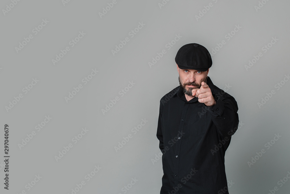 Handsome serious middle-aged man in a white shirt shows a finger at the camera on a gray background with copy space Handsome serious middle-aged man in a white shirt shows a finger at the camera on a gray background with copy space
