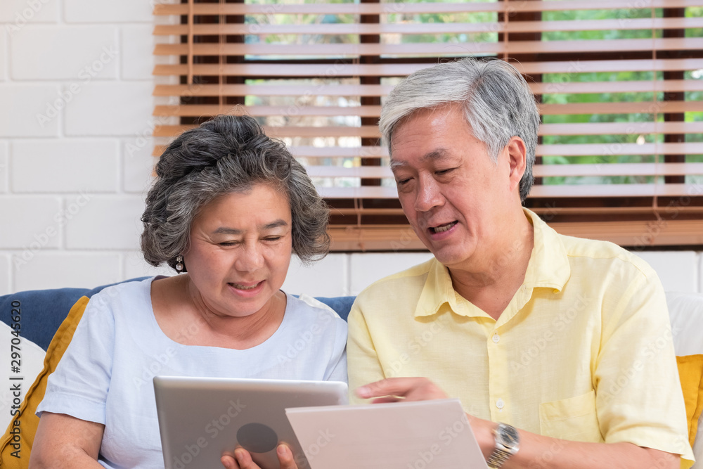 Fototapeta premium Asian senior couple use tablet searching about retirement financial document sitting on sofa at home,senior learn to use technology.aging in place concept