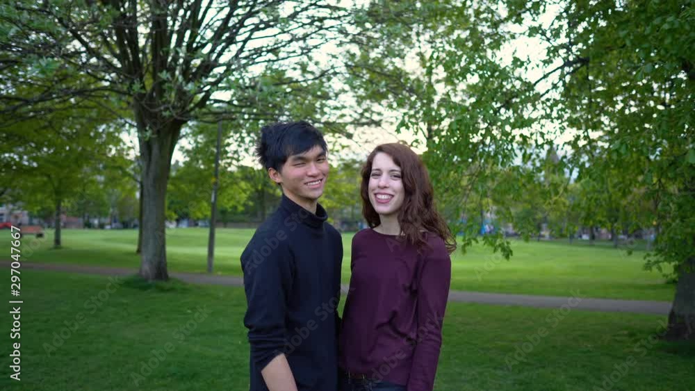 Confident Young Mixed Ethnecity Couple Portrait Standing in Park - Caucasian Woman and Asian Man Confident Young Mixed Ethnecity Couple Portrait Standing in Park - Caucasian Woman and Asian Man