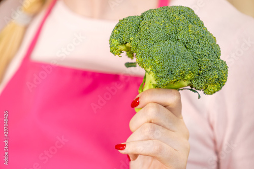 Woman in kitchen holding green fresh broccoli. Housewife cooking. Healthy eating, vegetarian food, dieting and people concept.