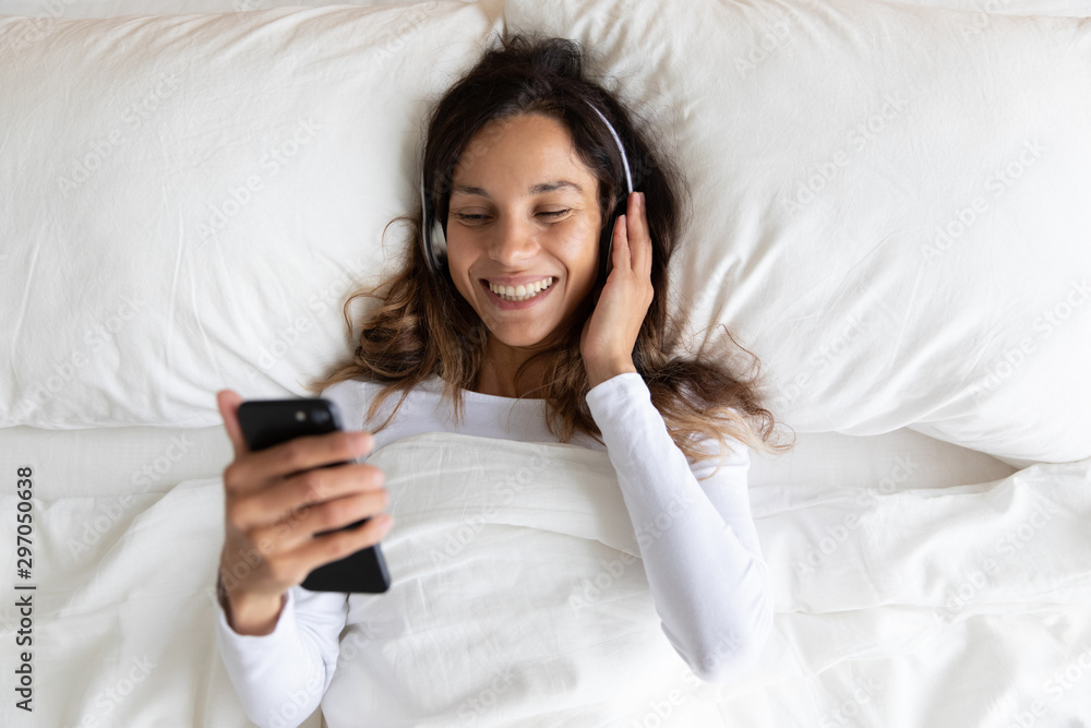 Happy millennial biracial woman lying in bed with headphones. Happy millennial biracial woman lying in bed with headphones.