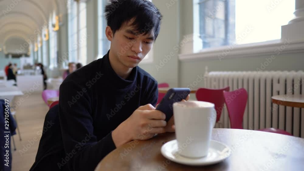 Young Asian Man Sitting at Cafe and Texting on Smartphone Young Asian Man Sitting at Cafe and Texting on Smartphone