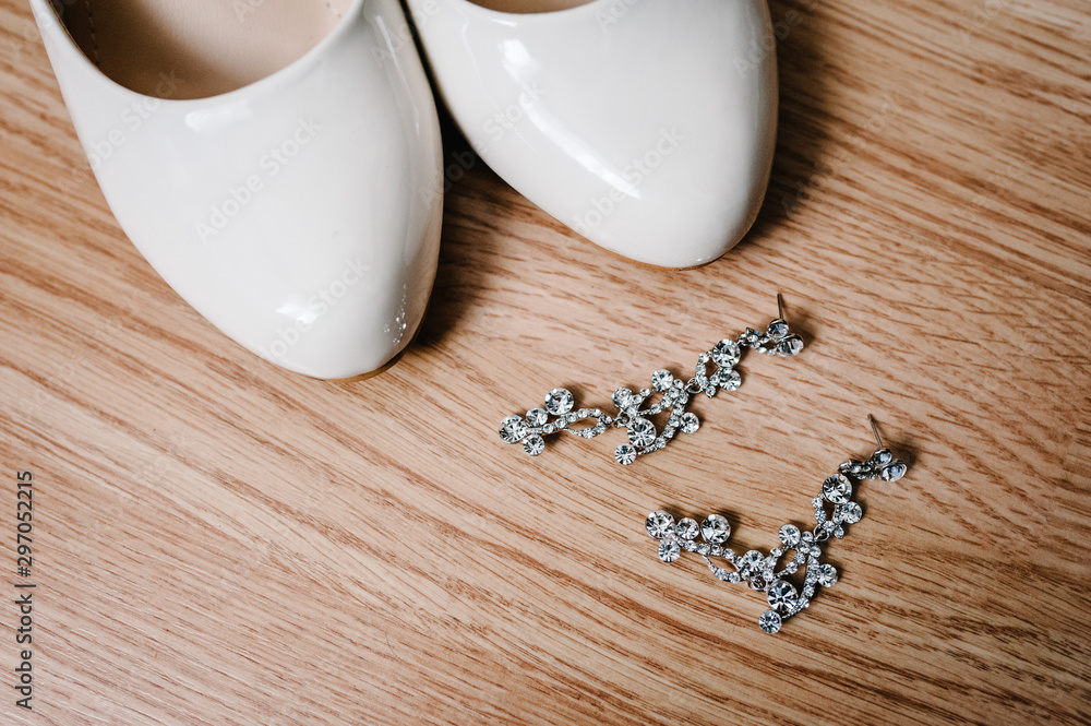 Part of women's stylish elegant classic lacquered beige shoes and two silver earrings lie on the pastel background. Isolated Wedding accessories for the bride. Part of women's stylish elegant classic lacquered beige shoes and two silver earrings lie on the pastel background. Isolated Wedding accessories for the bride.