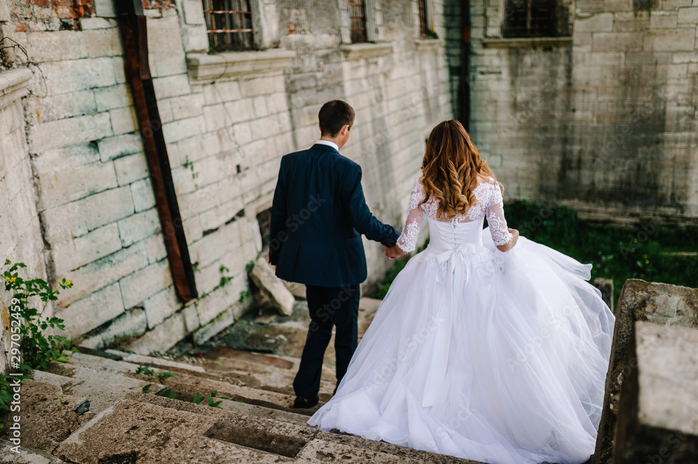 The bride and groom go back down the old stairs near antique, old castle, renaissance palace after the wedding ceremony. Rear view. The bride and groom go back down the old stairs near antique, old castle, renaissance palace after the wedding ceremony. Rear view.