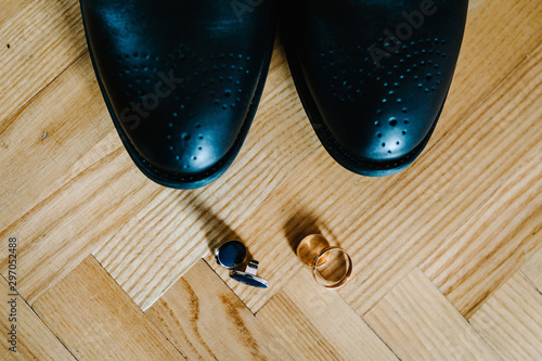 Part stylish men black shoes, cufflinks, wedding two rings lying on a light brown table. Wedding accessories groom on rustic wooden background. idea composition. holiday concept. flat lay. top view.