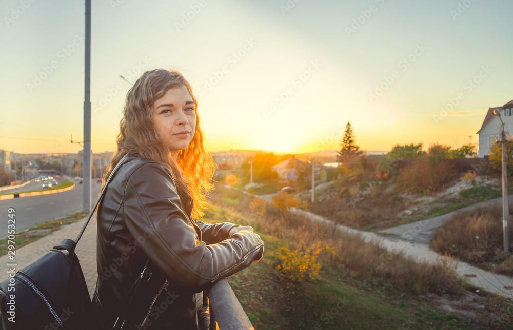 A beautiful woman stands on the bridge and looks at the sunset, looking thoughtfully. The girl is in a thoughtful mood. Woman standing alone, sunset.
