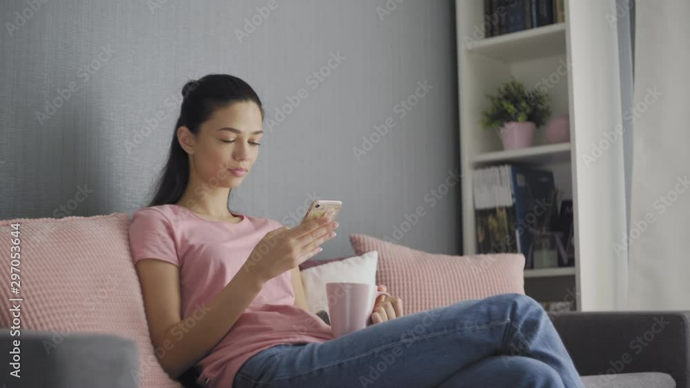 Young woman using the smartphone with touchscreen and drinking coffee in the early morning