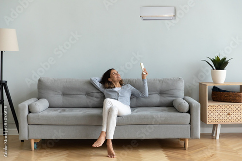 Joyful mixed race woman turning on cooler system air conditioner.