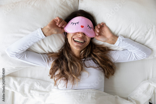 Happy millennial woman lying in bed with sleeping mask. photo