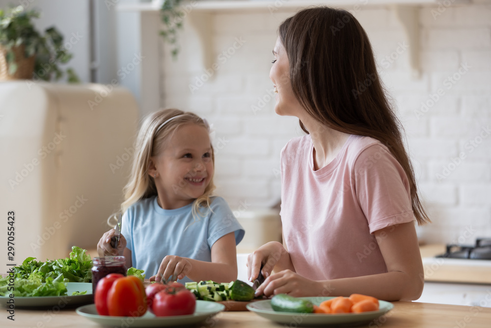 Happy mother and adorable little daughter preparing salad together