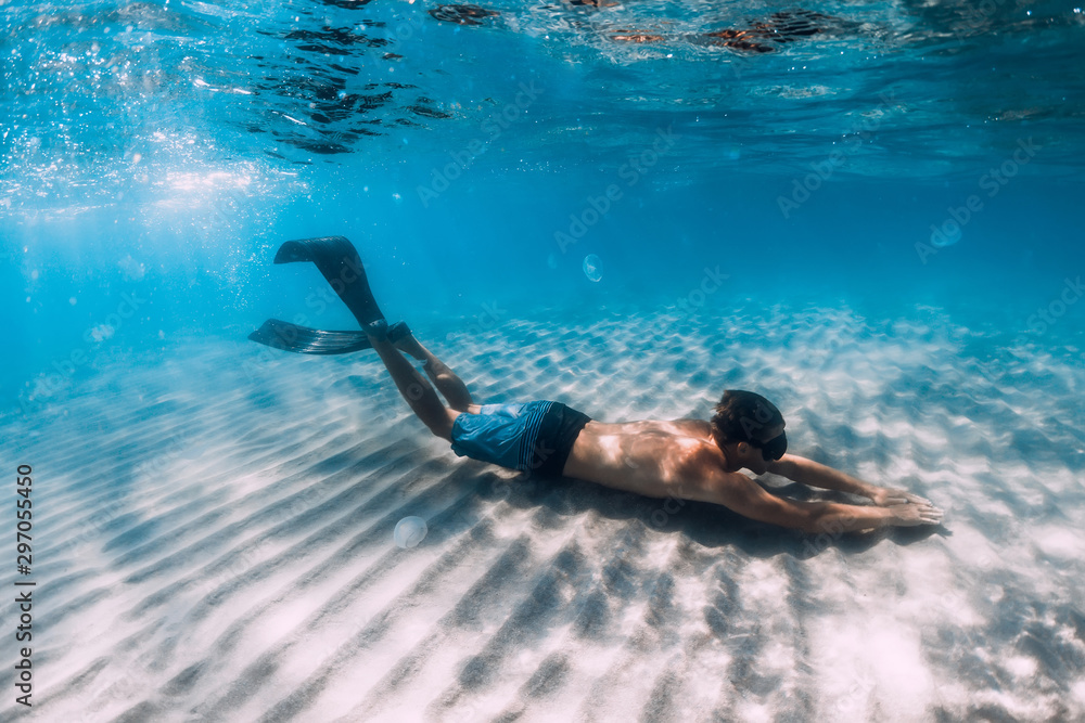 Freediver glides underwater over sandy bottom. Swimming with fins