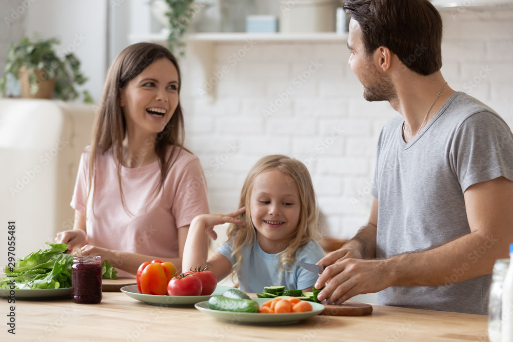 Happy family with little daughter preparing salad for dinner together