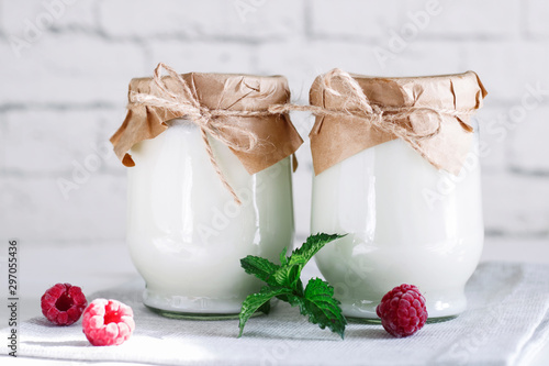 Organic probiotic milk kefir drink or yogurt in glass containers, with raspberry, on the white grey background. Gut health. Probiotic cold fermented dairy drink. Trendy food and drink. Copy space photo