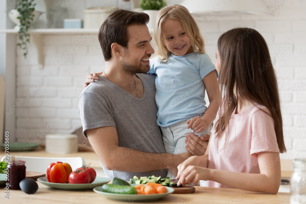 Smiling father holding little daughter, family preparing dinner in kitchen