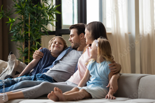 Happy family, mother, father and children hugging, relaxing on couch