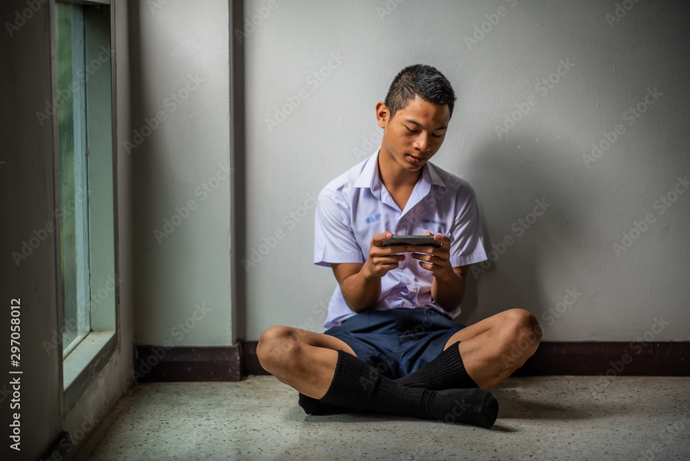 Male Asian high school student in white uniform addicted to online games.