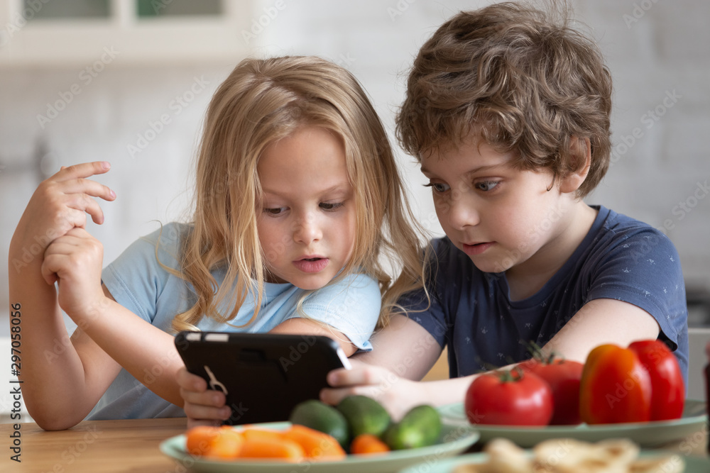 Curious little girl and boy using phone in kitchen Curious little girl and boy using phone in kitchen