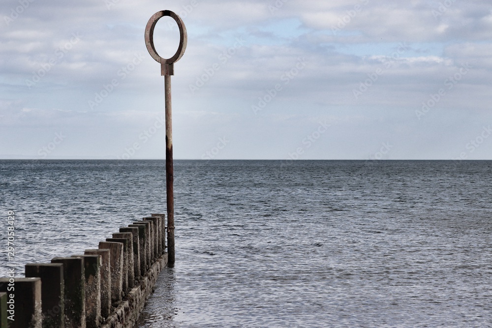 Beach groyne circular marking post overlooking the horizon
