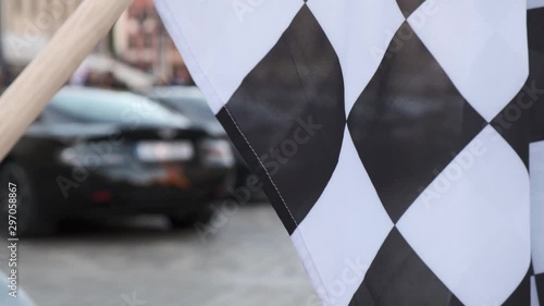 Modern luxury cars stand at the exhibition against the backdrop of a black and white racing flag.