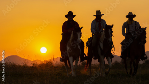 Three of Cowboys riding horses at sunset. © Samruay
