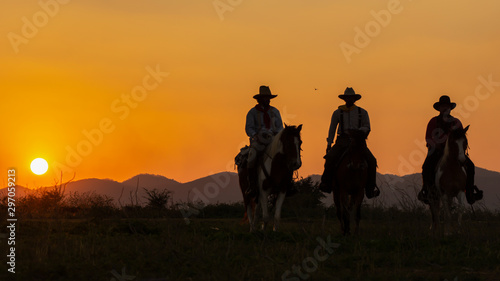 Three of Cowboys riding horses at sunset. © Samruay