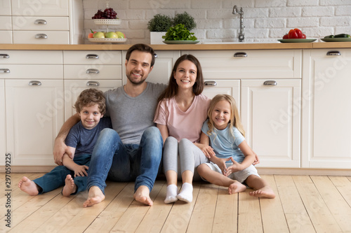 Portrait happy family hugging, sitting on warm floor in kitchen