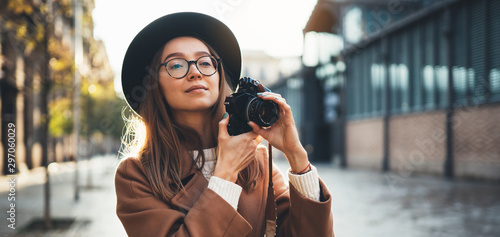 Hobby photographer concept. Outdoor lifestyle portrait of pretty young woman in sun city in Europe with camera travel photo of photographer in glasses and hat take photo copy space mockup photo