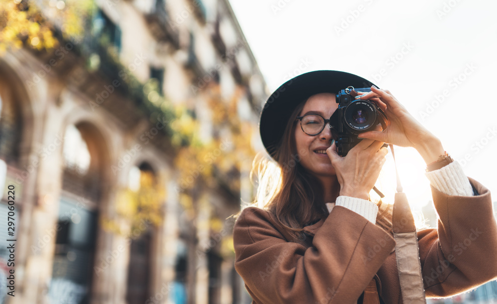 Photographer in glasses with retro photo camera. Tourist portrait girl in hat travels in Barcelona holiday. Sunlight flare street in europe city. Traveler hipster shoot architecture, copy space mockup