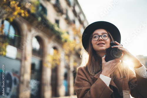 Photographer with retro photo camera. Tourist portrait. Smile girl in hat travels in Barcelona holiday. Sunlight flare street in europe city. Traveler hipster shooting architecture, copy space mockup
