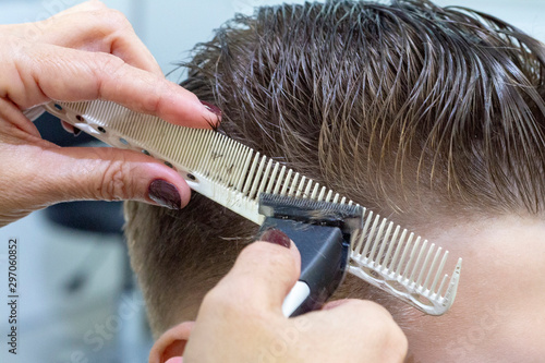 Sliding rear view shot of a barber using a clipper giving a haircut to male client. Cropped shot of a professional hairstylist shaving of the head of unrecognizable young man