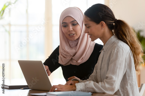 Asian muslim female mentor teaching caucasian intern explaining computer work photo