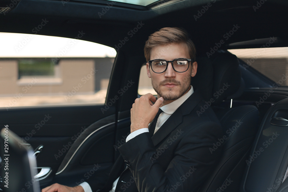Thoughtful confident businessman in full suit with eyewear looking away while sitting in the car. Thoughtful confident businessman in full suit with eyewear looking away while sitting in the car.