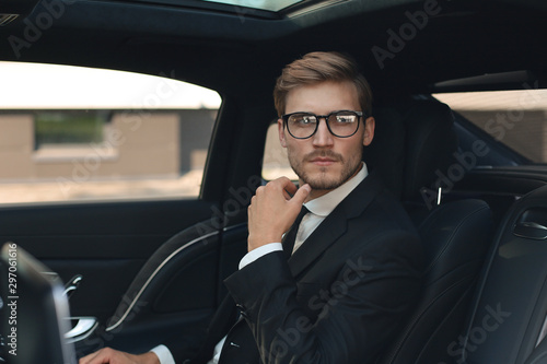 Thoughtful confident businessman in full suit with eyewear looking away while sitting in the car. © ty