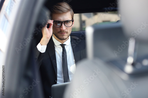 Thoughtful confident businessman keeping hand on glasses while sitting in the luxe car.