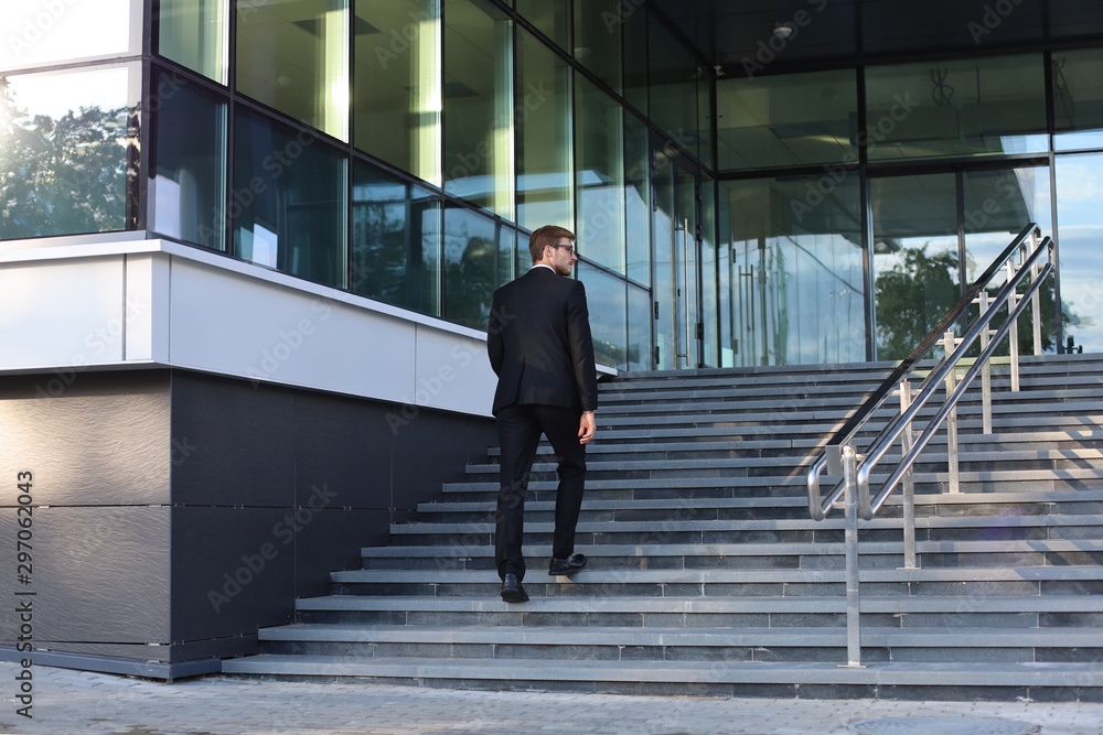 Stylish successful businessman goes up the stairs of the office building.