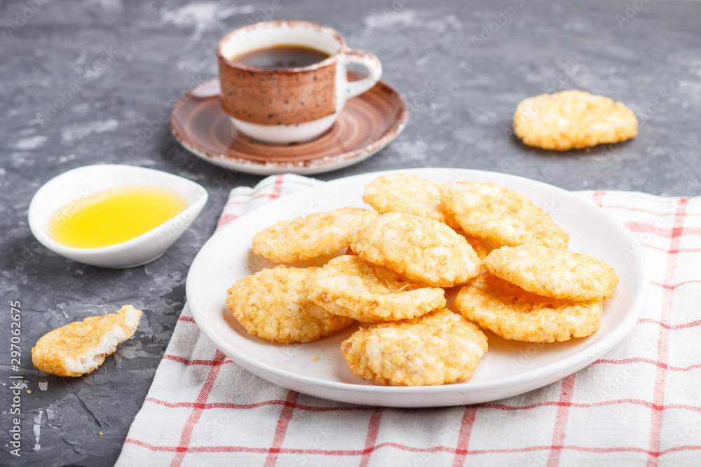 Traditional japanese rice chips cookies with honey and soy sauce on a white ceramic plate and a cup of coffee on a black concrete background. side view, selective focus. Traditional japanese rice chips cookies with honey and soy sauce on a white ceramic plate and a cup of coffee on a black concrete background. side view, selective focus.