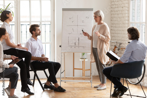 Fotografie Skilled old female mentor give presentation training staff at meeting