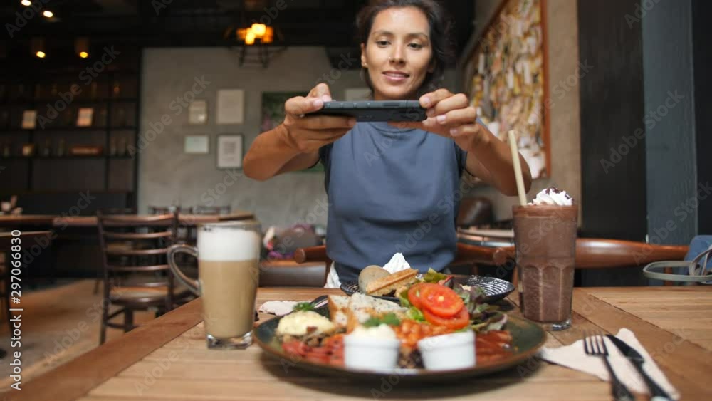 Smiling Mixed Race Woman Taking Photo of Healthy Breakfast Using Mobile Phone in Vegan Restaurant. 4K Slowmotion Flatlay Food Photography on Wooden Table in American Diner. Thailand. Smiling Mixed Race Woman Taking Photo of Healthy Breakfast Using Mobile Phone in Vegan Restaurant. 4K Slowmotion Flatlay Food Photography on Wooden Table in American Diner. Thailand.