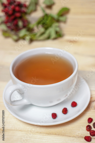 White cup of tea with plate and dry rowan berries wooden background vertical