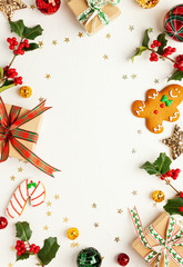 Christmas background with gingerbread cookies, gift boxes and branches of holly with red berries on white. Winter festive nature concept. Flat lay, copy space.