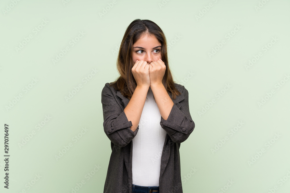Young brunette girl with blazer over isolated green background nervous and scared putting hands to mouth Young brunette girl with blazer over isolated green background nervous and scared putting hands to mouth